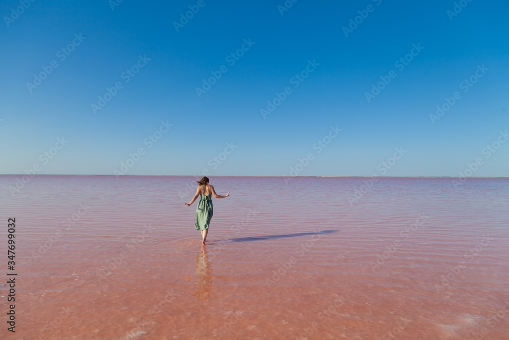 Woman in dress stands in rose water lake against blue sky