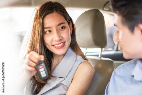 Happy Asian young woman showing remote car to her friend at automotive rental, customer satisfied feedback, test driving, dealership or purchasing concept, back to normal life after Coronavirus end. 