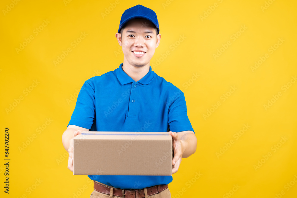 Delivery express of portrait asian male fast deliver to receiver carrying carton shipping buying online order wearing blue uniform on yellow background isolated studio shot. Delivery express of portrait asian male fast deliver to receiver carrying carton shipping buying online order wearing blue uniform on yellow background isolated studio shot.