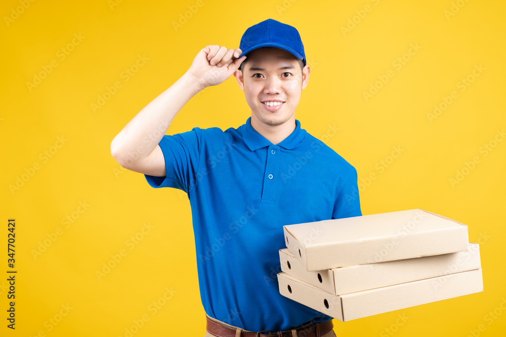 Delivery express of pizzaman asian male showing box delicious fast deliver to receiver shipping buying online order wearing blue uniform on yellow background isolated studio shot. Delivery express of pizzaman asian male showing box delicious fast deliver to receiver shipping buying online order wearing blue uniform on yellow background isolated studio shot.