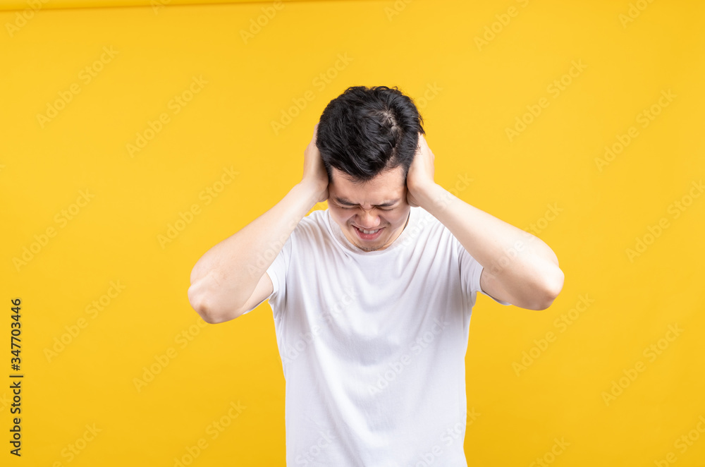 Attractive young asian man covering your ears loud noise shouting mouth angry and fury negative emotion wearing white t-shirt on yellow background isolated studio shot with copy space Attractive young asian man covering your ears loud noise shouting mouth angry and fury negative emotion wearing white t-shirt on yellow background isolated studio shot with copy space
