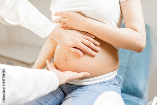 Male doctor makes a massage of the abdomen of pregnant woman during a medical examination, cropped view without face focused on the belly and hands