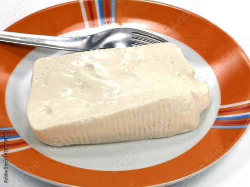 Closeup shot of soft cheese of bovine stracchino on a plate on a white isolated background