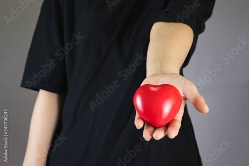 human in a black T-shirt stretched out his hand, holding the red plastic heart out the front.Selective focus