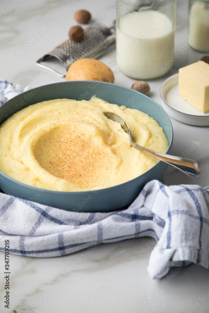 Schale Schüssel mit Kartoffelpüree mit Zutaten aus Kartoffeln, Milch, Salz, Butter, Muskatnuss dazu Küchentuch und Muskatreibe auf hell Marmor Hintergrund Schale Schüssel mit Kartoffelpüree mit Zutaten aus Kartoffeln, Milch, Salz, Butter, Muskatnuss dazu Küchentuch und Muskatreibe auf hell Marmor Hintergrund