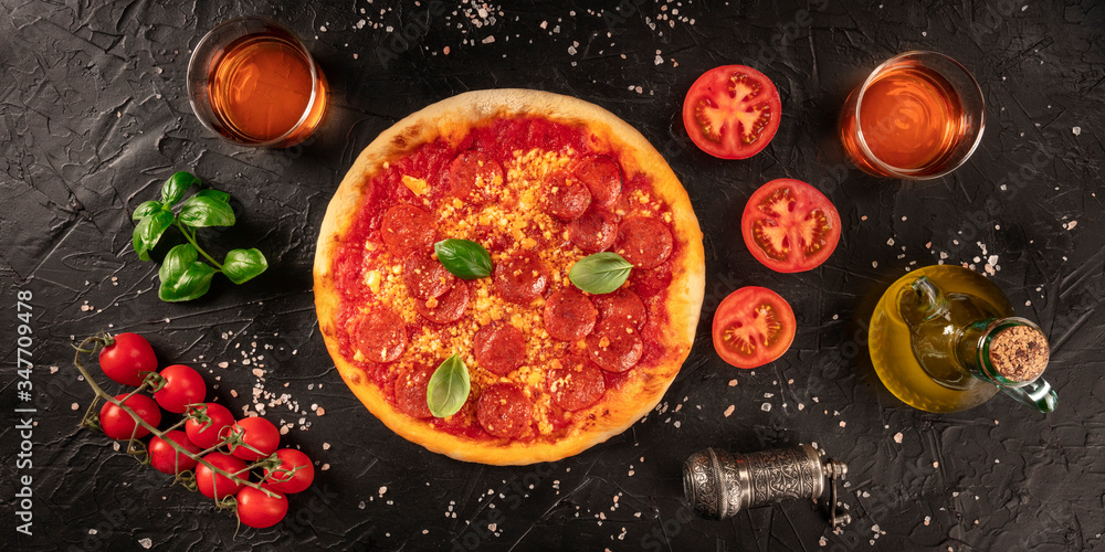 Pepperoni pizza panorama on a dark background, with wine and ingredients, tomatoes, basil, and olive oil, overhead shot
