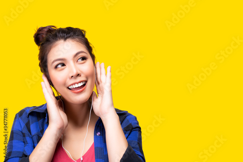 Smiling young asian woman listening music, look at copy space. Teen use technology wireless earphones. isolated yellow color background, copy space. Lifestyle, leisure activity concept. colorful life