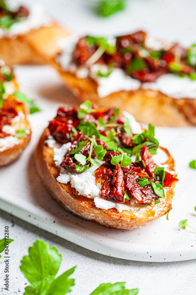 Toasts with sun-dried tomatoes and cream cheese on white board, white background.