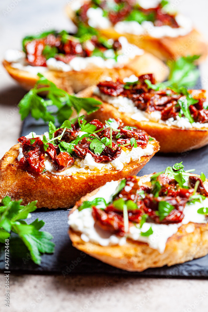 Toasts with sun-dried tomatoes and cream cheese on black board, dark background.