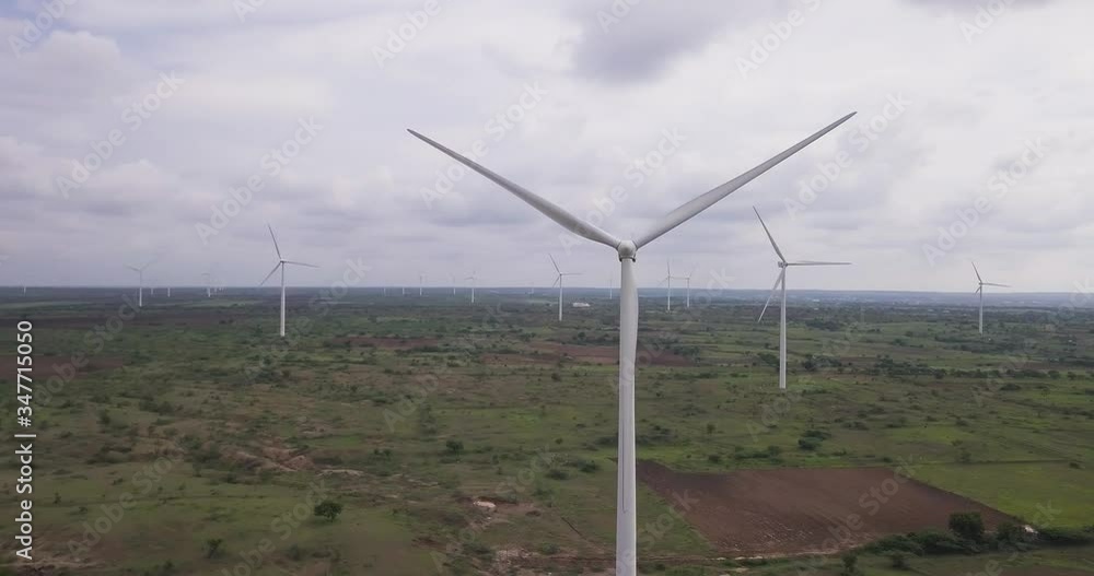 Scenic aerial view of fast spinning wind turbines in the rural landscape of Karnataka, India. Wind farm producing sustainable energy. Scenic aerial view of fast spinning wind turbines in the rural landscape of Karnataka, India. Wind farm producing sustainable energy.