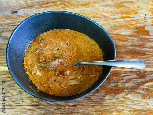 top view of portion of homemade Oxtail soup in black bowl on shabby wooden table at home kitchen photo