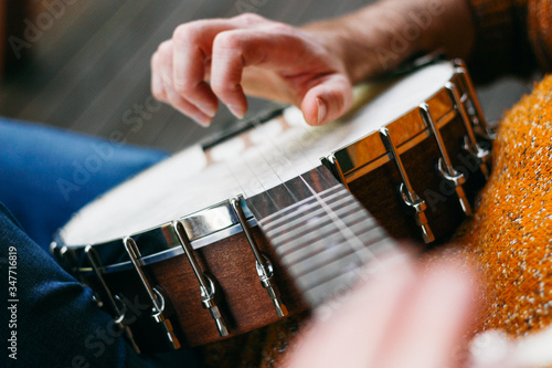 Fotografi Close up of a male banjo player relaxing on the porch, practicing clawhammer, finger picking and thumb tapping