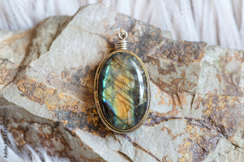 Brass pendant with natural labradorite gemstone on rocky background