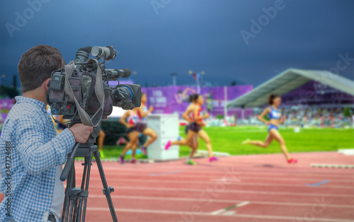 Cameraman shooting live broadcast from athletics game to television and internet on the background blured Unidentified women athletes  photo