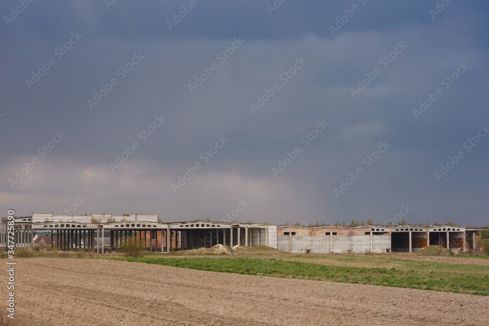 Ruins of an industrial building on a background of stormy sky. Sown fields in the foreground Ruins of an industrial building on a background of stormy sky. Sown fields in the foreground