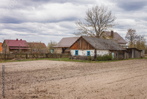 Picturesque rural landscape with a plowed field and an old wooden house beside it. Cloudy day