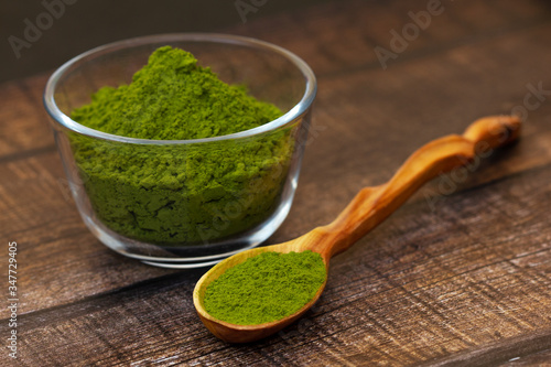Fototapeta Naklejka Na Ścianę i Meble -  Green tea matcha in a glass bowl and a spoon on a brown wooden background close-up. Matcha in a wooden spoon.