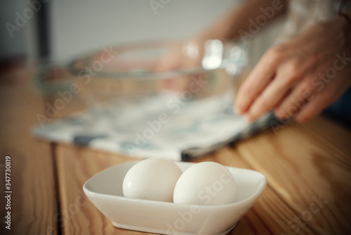 Two raw eggs in a bowl close-up on a background of a bowl and hands of a pastry chef