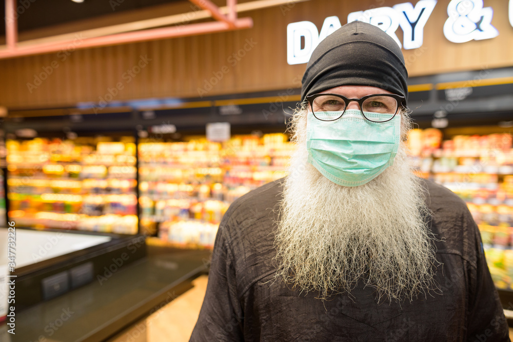 Face of mature bearded hipster man with mask social distancing at the supermarket
