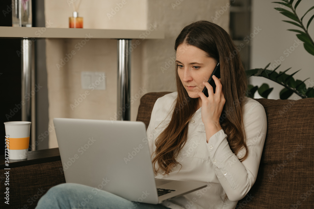 Remote work. A caucasian woman working remotely on her laptop. A businesswoman doing business with her smartphone sitting on the couch.. Remote work. A caucasian woman working remotely on her laptop. A businesswoman doing business with her smartphone sitting on the couch..