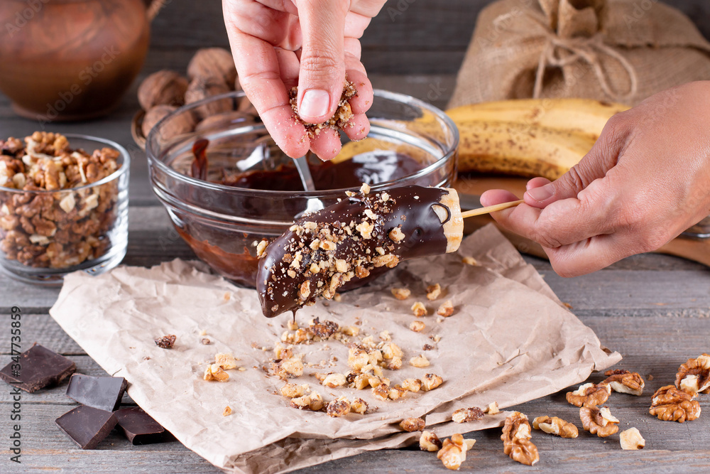 Woman hands sprinkle nuts on a frozen banana. Frozen Chocolate Bananas on a Stick