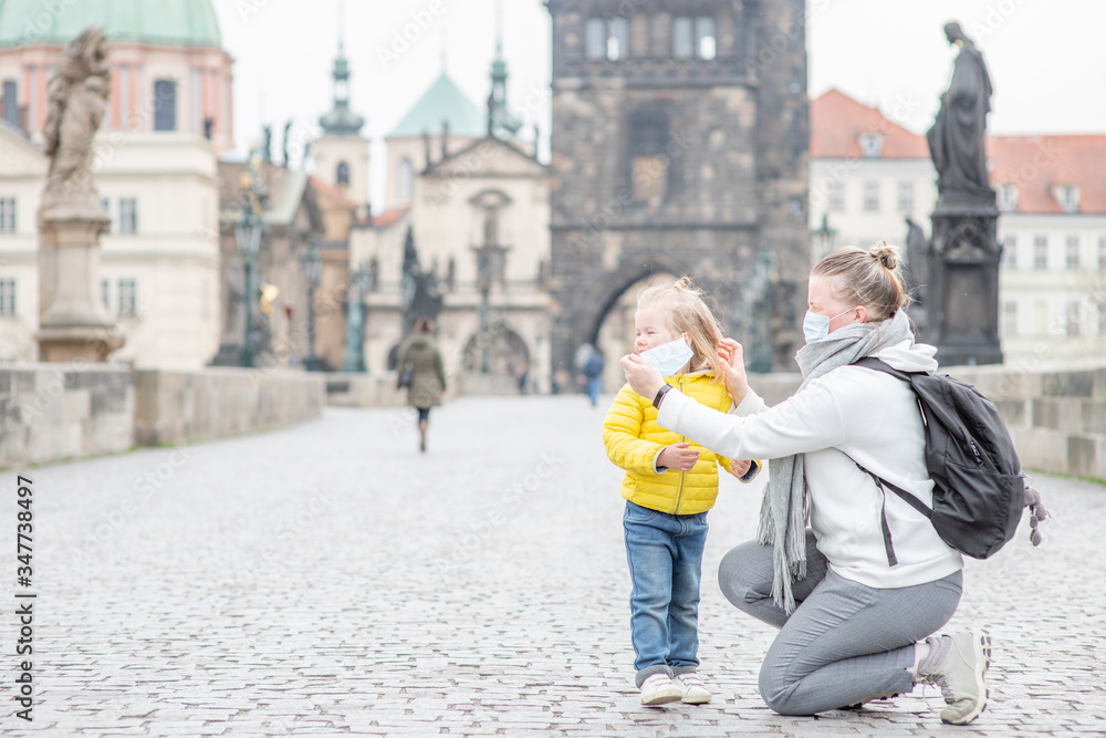 Mother puts on her little daughter a medical mask on Charles Bridge in Prague. Coronavirus epidemic concept. Empty space for text