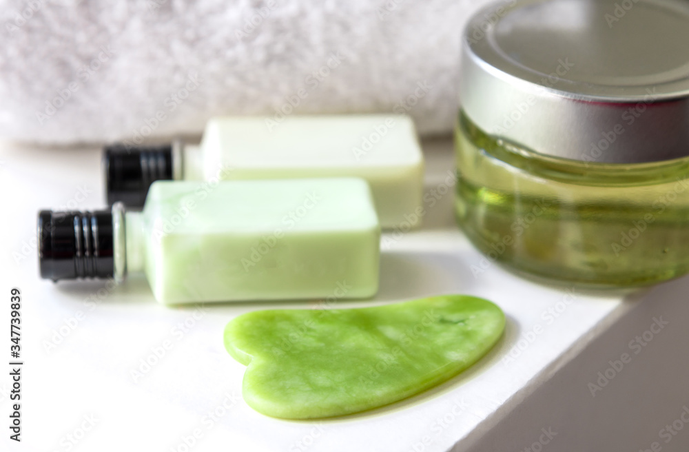 Green gua sha tool with cosmetic products at background. Selective focus Green gua sha tool with cosmetic products at background. Selective focus