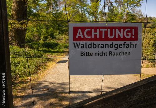Text sign in German: Caution, danger of forest fires. Please do not smoke. Sign in red and white in the background of a forest path