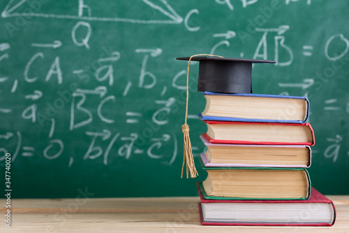 Graduation cap with books on the chalkboard background in the auditorium