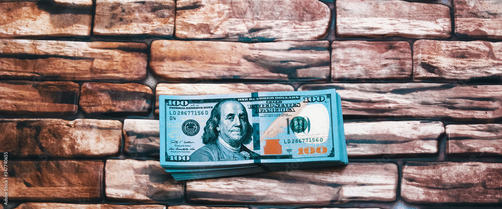 A pack of dollars.A large wad of hundred-dollar bills is lying on a brick wall of dark red brown color.