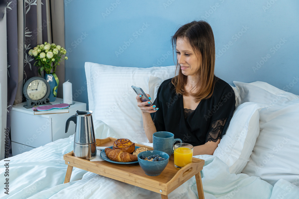 Morning of handsome young woman talking by smartphone during breakfast in bed Morning of handsome young woman talking by smartphone during breakfast in bed