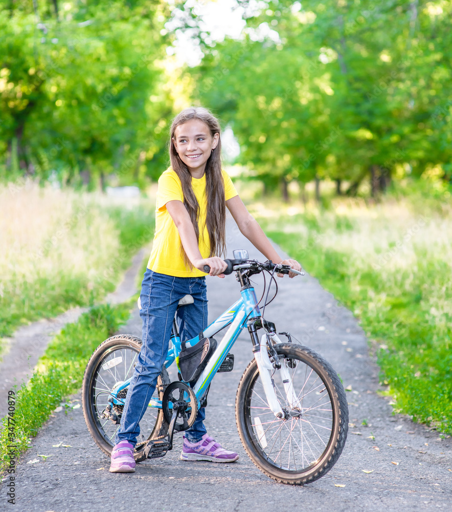 Fototapeta premium Portrait of a young happy girl standing with her bike in a summer park. Activity leisure concept
