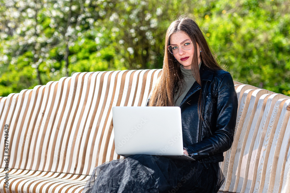 young woman in eyglasses sitting on bench in park with laptop computer and looking at the camera young woman in eyglasses sitting on bench in park with laptop computer and looking at the camera