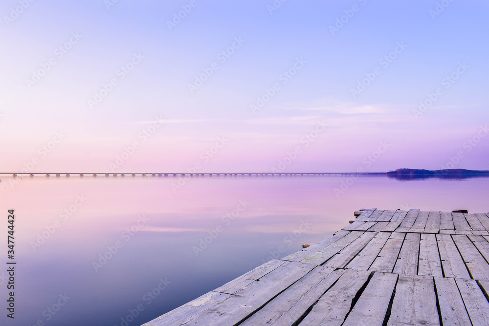Pier on the background of the sea with a glossy surface, which reflects the pink-blue sky