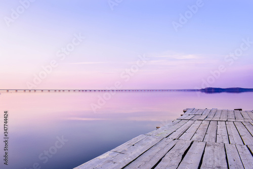 Fototapeta Naklejka Na Ścianę i Meble -  Pier on the background of the sea with a glossy surface, which reflects the pink-blue sky