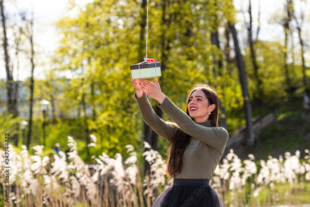 Naklejka premium on a sunny and windy day young smiling emotional brunette receives a surprise gift delivered by quadcopter, concept of modern fast delivery method