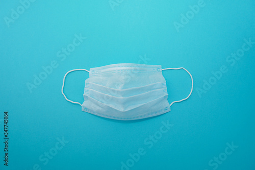 Disposable medical surgical face mask on blue background. Coronavirus (COVID-19) pandemic. Stay home, stay safe