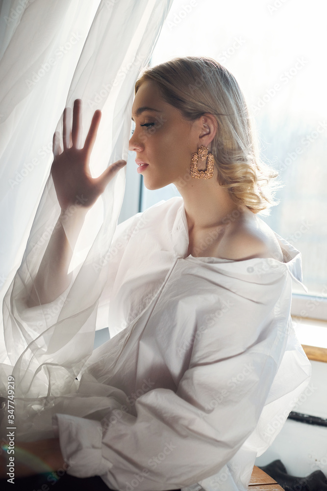 Naklejka premium Blonde women with jewelry earrings in their ears in the rays of the evening sun. Beauty face long hair clean smooth skin, natural cosmetics and makeup