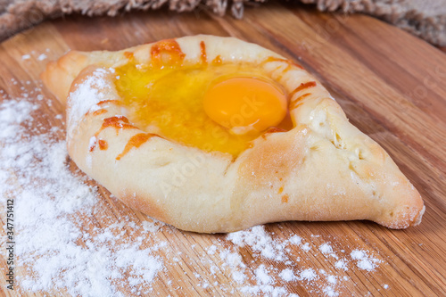 Adjarian khachapuri on the wooden floured cutting board close-up photo