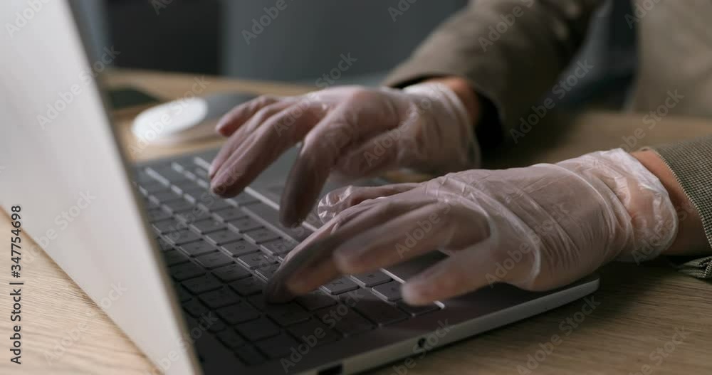 Close up of Caucasian female hands in rubber gloves typing and tapping on keyboard laptop computer in office on desk. Wooden table. Coronavirus pandemic protection concept. Close up of Caucasian female hands in rubber gloves typing and tapping on keyboard laptop computer in office on desk. Wooden table. Coronavirus pandemic protection concept.