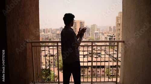 Young man clap hands in balcony window to thank, applaud doctors, health workers, nurses, police on Janata curfew day during coronavirus outbreak in Mumbai, Maharashtra, India, 22 March 2020 photo