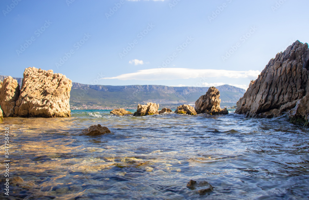 View of a small hidden beach on the adriatic sea. View low down on the bright clear water surrounded by rocks. Mountains and towns in the distance