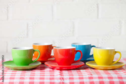 Colorful cups on the white background of a brick wall. Background with copy space. Horizontal. Selective focus.
