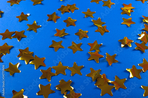 Gold shiny confetti in the shape of stars on a bright blue background. Festive and Christmas background. Top view  copy space