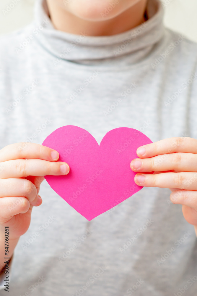 Closeup of pink heart in hands of little girl on white background. Child is holding pink heart.