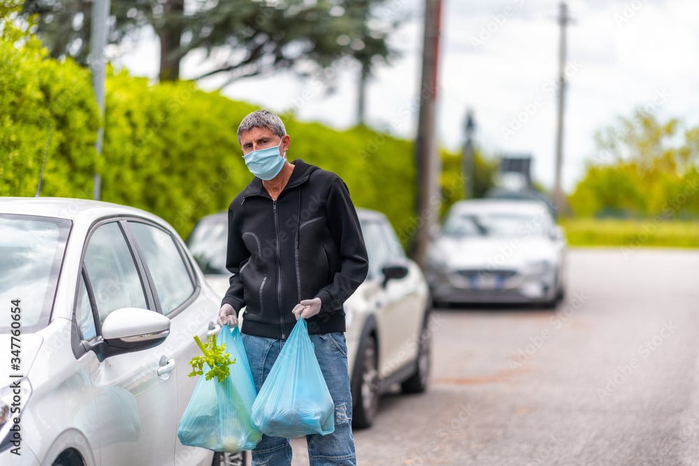 Man wearing mask in coronavirus times holding groceries bag near his car Man wearing mask in coronavirus times holding groceries bag near his car
