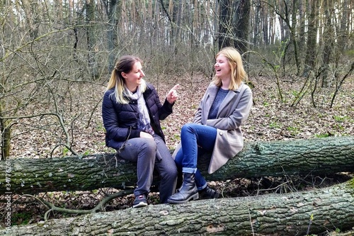 European women sit on log and talk at spring forest