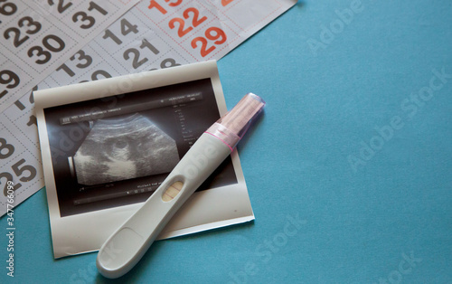 Ultrasound scan of an unborn baby of fifth week with a pregnancy test and calendar on the blue background. Pregnancy concept. 
