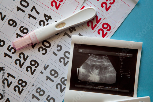 Ultrasound scan of an unborn baby of fifth week with a pregnancy test and calendar on the blue background. Pregnancy concept. 
