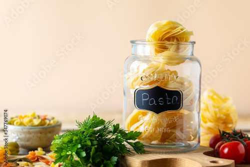 Different types of italian pasta in glass jars on a yellow wooden table. copy space. Diet and nutrition concept.